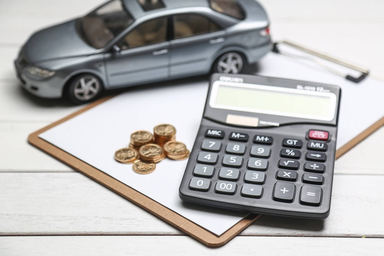 Calculadora, moedas e carrinho de brinquedo em cima de uma mesa, representando o cálculo de isenção do IP`VA para Uber